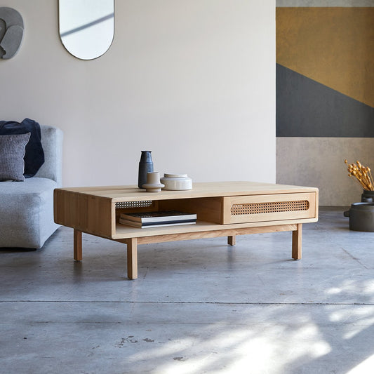 A rectangular Louis Coffee Table with natural rattan cane work, placed in a living room setting, with a plant, mirror, and furniture in the background.